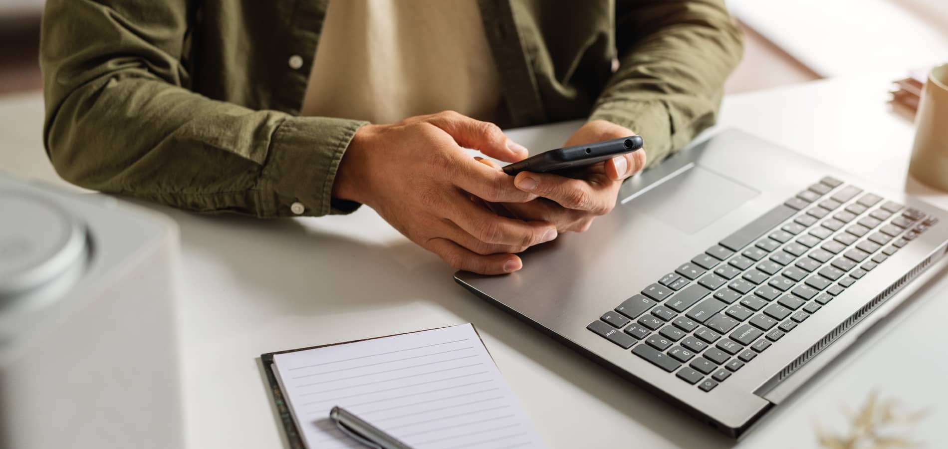 image of a man on his phone in front of an open laptop